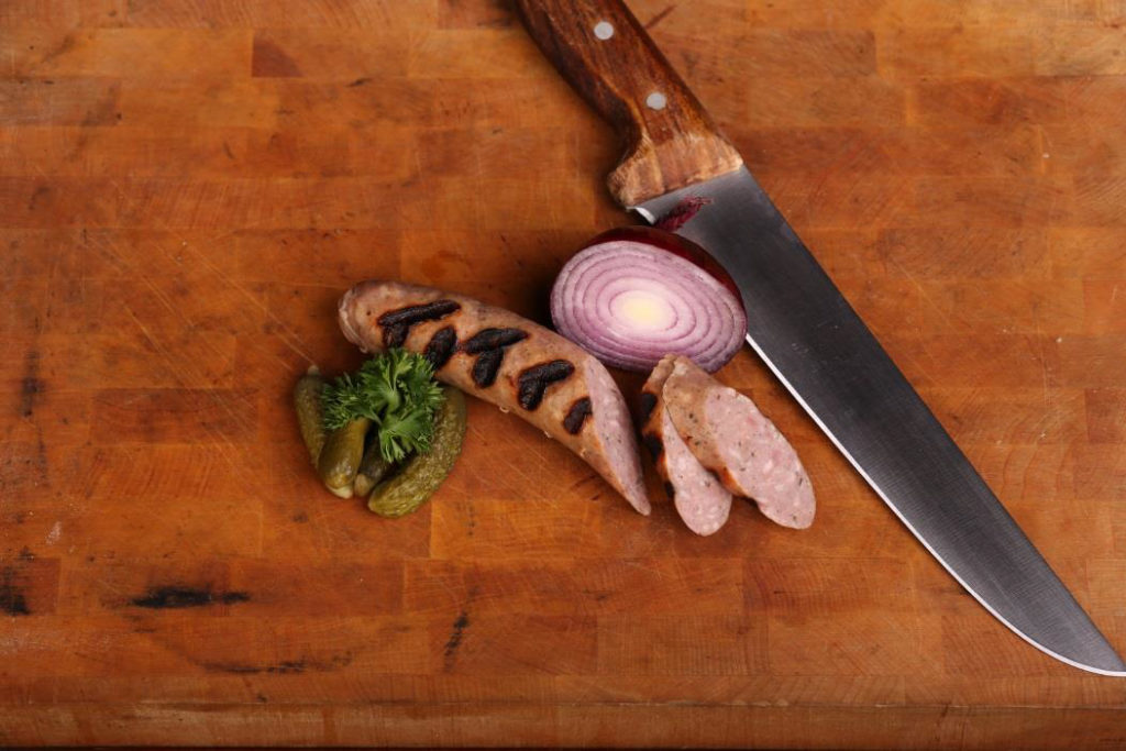 Korv på en bricka tillsammans med gurka, lök och en kniv